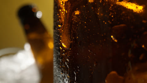 Nahaufnahme-Von-Kondensationstropfen,-Die-An-Glasflaschen-Mit-Kaltem-Bier-Oder-Alkoholfreien-Getränken-Herunterlaufen,-Die-In-Einem-Mit-Eis-Gefüllten-Eimer-Vor-Gelbem-Hintergrund-Gekühlt-Werden